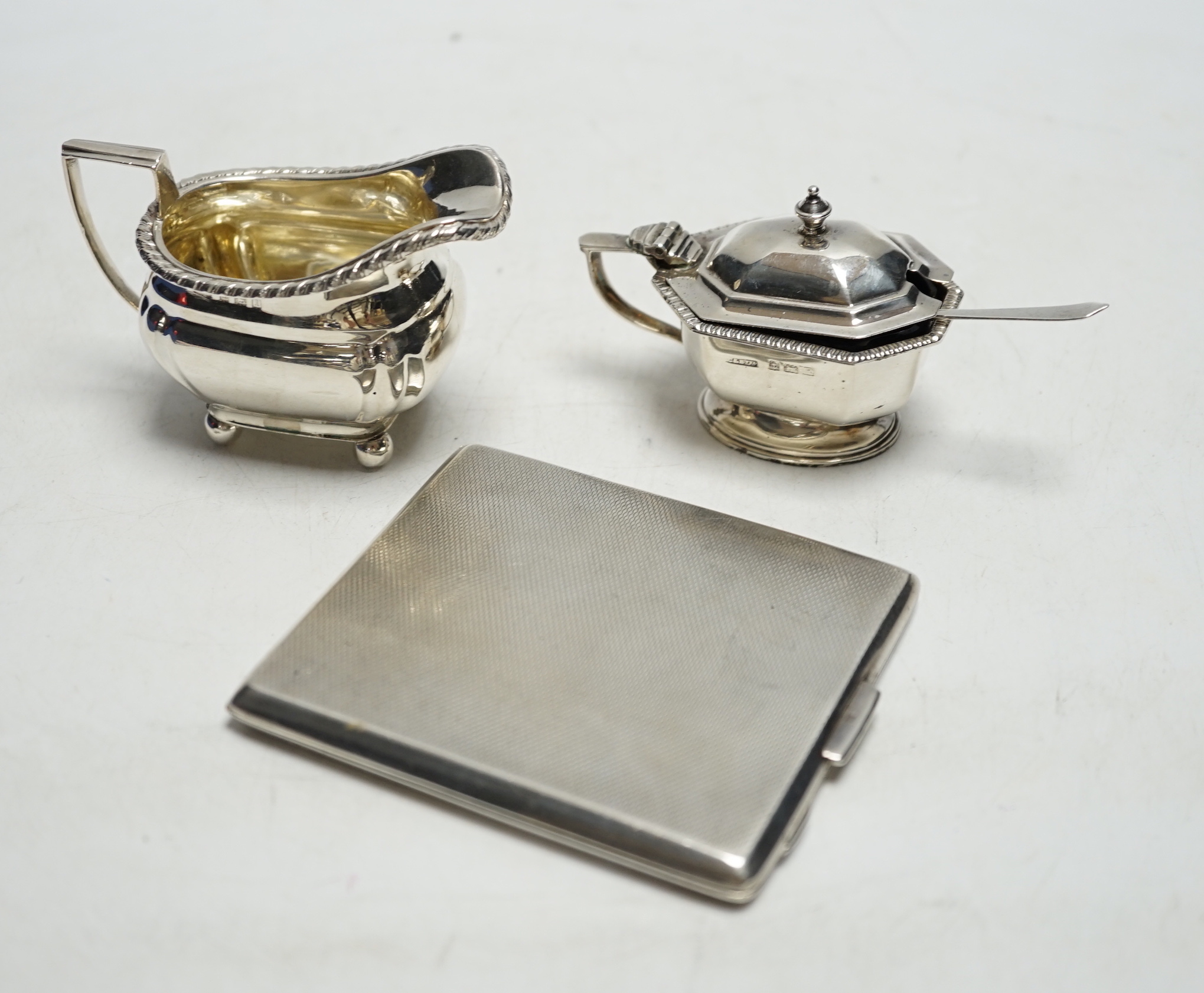 A George VI engine turned silver cigarette case, a silver lidded mustard pot and a small silver cream jug.